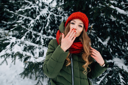 美丽的女人在冬日的雪林中用相机送吻