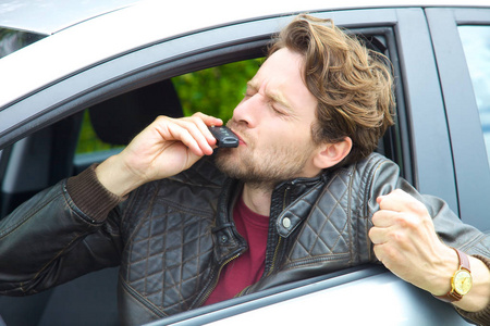 英俊的快乐的男人在车上亲吻钥匙的新车