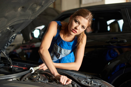 特写的黑发女性技工修理或检查一辆汽车, 手里拿着一个扳手。女孩穿着工作服