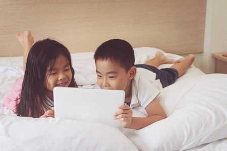 亚洲的小的男孩和女孩在床上使用平板电脑