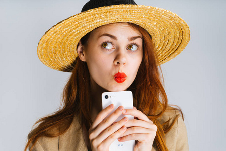 一个有趣的女孩，在一顶帽子和红色的嘴唇是拿着手机，看着别处