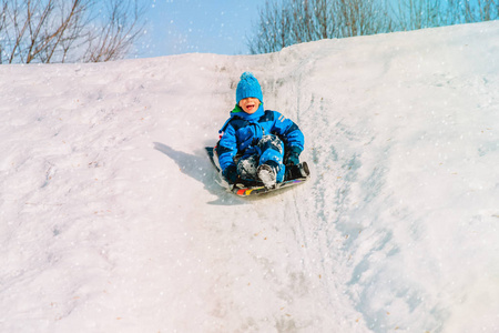 孩子们冬天好玩滑动在雪地里的小男孩