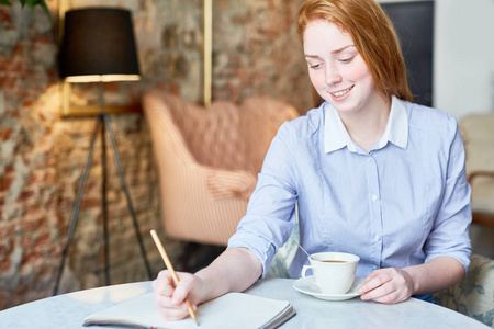 创意 redhaired 女孩用铅笔和笔记本思考的想法杯咖啡