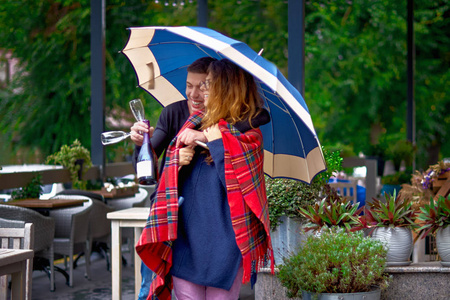 一对年轻的情侣在阳台上拥抱着雨伞, 手里拿着香槟的家伙。约会概念