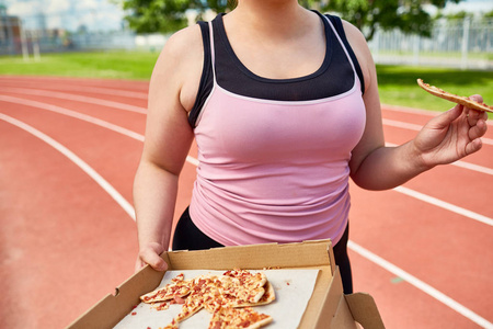 黑色和粉红色的胖女人 tanktops 在体育场的训练中吃比萨饼切片