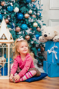 金发碧眼的小女孩坐着, 微笑着几乎装饰圣诞树