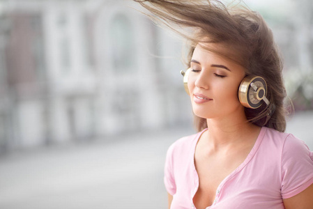 美丽的年轻女子，与老式的音乐耳机，站在城市背景下和听音乐
