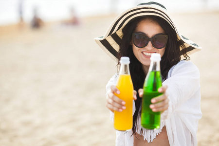 坐在沙滩上的年轻女子和在海滩上举行黄色和绿色鸡尾酒