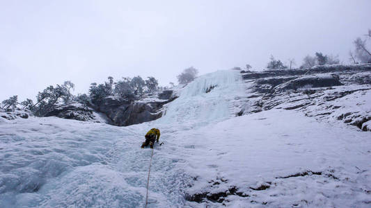 在阿尔卑斯寒冷的冬日, 雄山导游爬上陡峭的冰冻瀑布
