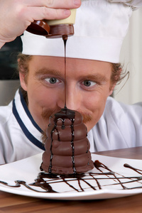 有趣的年轻厨师在一块蛋糕加巧克力酱