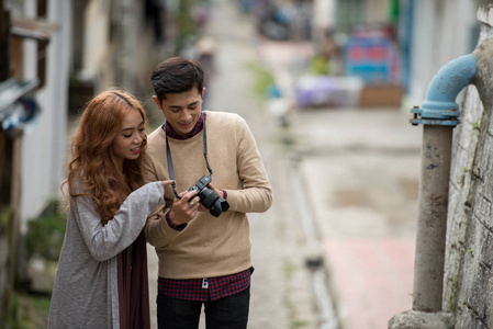 年轻的亚洲情侣看着他们在小城之旅拍摄的照片