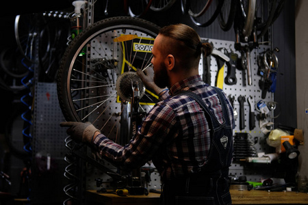 英俊时尚的男性穿着法兰绒衬衫和牛仔裤套装, 在修理店与自行车车轮工作