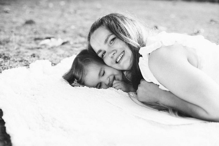 美丽的年轻母亲的肖像与她可爱的小女儿躺在夏季公园白色格子, 黑白相间
