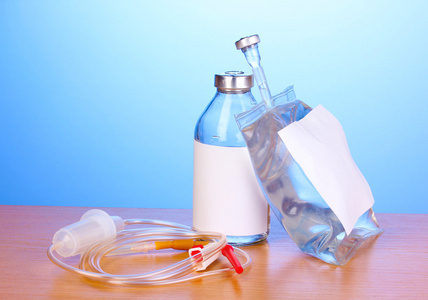 瓶和静脉注射抗生素和设置在蓝色背景上的木桌上的塑料输液袋