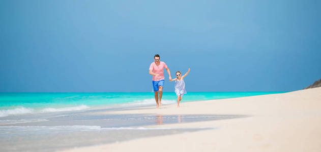 在热带海滩快乐的父亲和他可爱的小孩子的全景一起乐趣