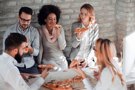 快乐的年轻的商业团队在办公室吃比萨饼。商业食品和人的概念