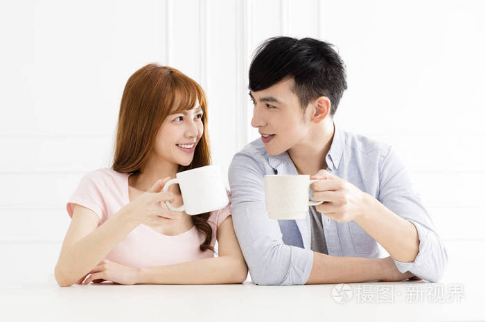 年轻的亚洲夫妇在客厅里喝咖啡