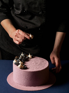 特写的女性手装饰美味的粉红色慕斯蛋糕与巧克力糖果在黑暗的背景下