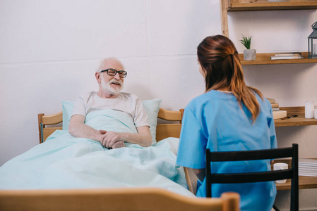 在床上微笑老患者与护士谈话