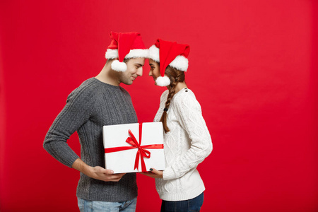 圣诞节概念被隔绝的可爱的年轻夫妇紧紧地拿着白色礼物在红色背景下