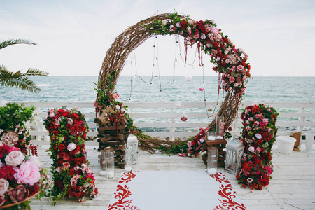 美丽的婚礼仪式在粉红色, 勃艮第和白色色调的木码头装饰。蓝海旁玫瑰和牡丹花组成的细枝圆拱