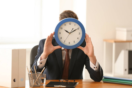 在办公室的桌子上, 一个人躲在钟后面。时间管理概念