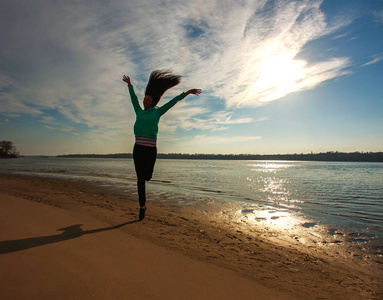 妇女跳在海滩在日出天空背景, 自由概念
