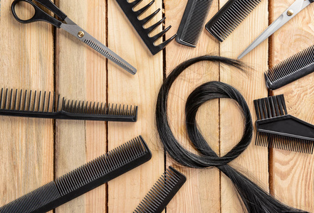 在木质背景下, 用美发师的工具和黑头发的绞线组成的平躺组合