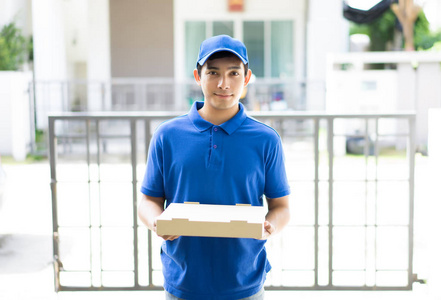 快乐送货人在蓝色制服举行比萨饼盒站立