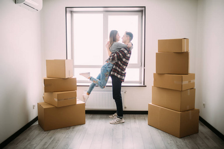 美丽的年轻夫妇的全长肖像拥抱和微笑, 而站在移动纸板箱在空房间里
