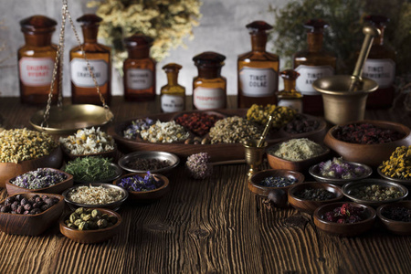 自然医学背景。黄铜砂浆, 瓶子。质朴的桌子。各式干草药在碗里。散景
