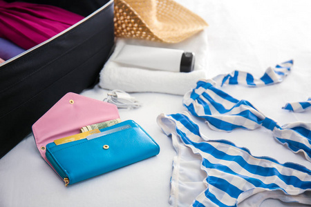 钱包, 泳装和打开行李箱与包装的东西在床上