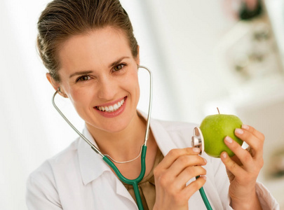 快乐的内科医生用听诊器检查苹果的女人