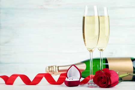 香槟瓶带眼镜, 红玫瑰和银色戒指在木桌上