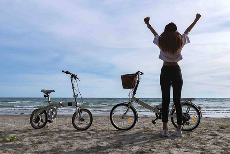 美丽的年轻女子骑自行车与白色的沙滩和大海在背景