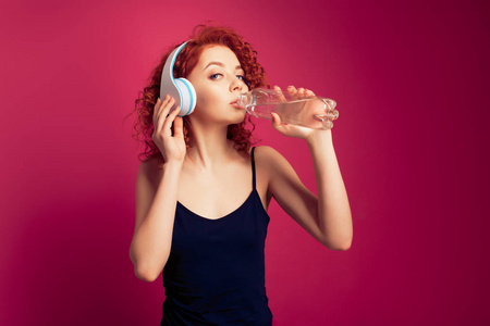 漂亮健康的年轻女子饮用纯矿泉水瓶装水在粉红色的背景