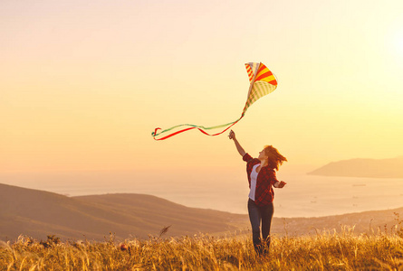 夏天日落时, 快乐的年轻女子带着风筝奔跑在空地上