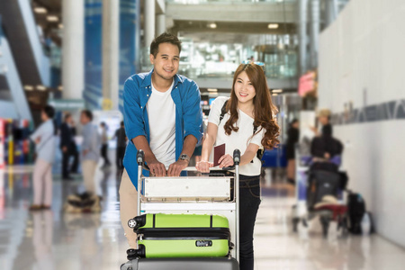 旅行者对亚裔夫妇与行李箱在机场。情人旅行和运输技术概念