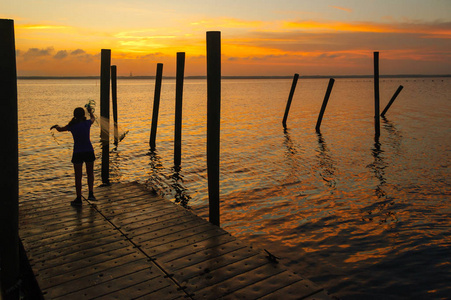 日落在荡漾的水与一个剪影女孩铸造网从船坞在前景