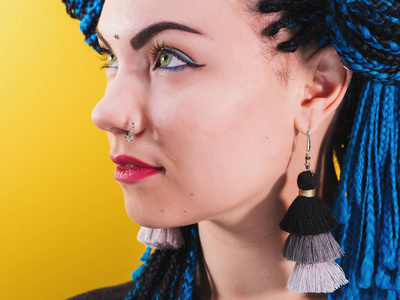 女人的魅力肖像与非洲蓝色辫子发型, 宾迪, 鼻环和流苏耳环在黄色背景下隔离