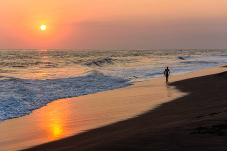 男性冲浪者在海滩上漫步日落的剪影