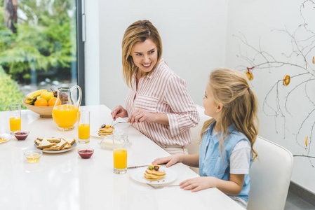 微笑的母亲和女儿在家一起吃早餐