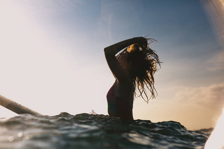 在海洋冲浪板上的女人调整头发的剪影
