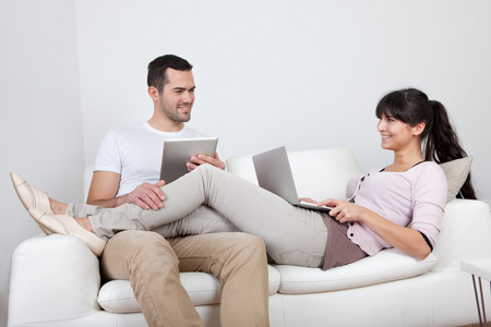 年轻的夫妇在沙发上使用笔记本电脑