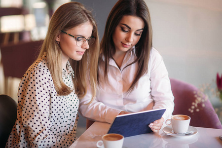 两个女孩坐在咖啡馆里喝咖啡时用平板电脑