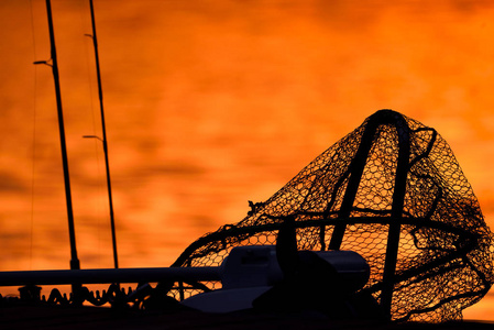 trollingmotor, 着陆网和钓鱼竿的剪影在一个码头在红色日落光在晚10月傍晚在芬兰南部