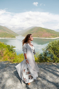 美丽的女孩在一条长的礼服在湖和山的背景