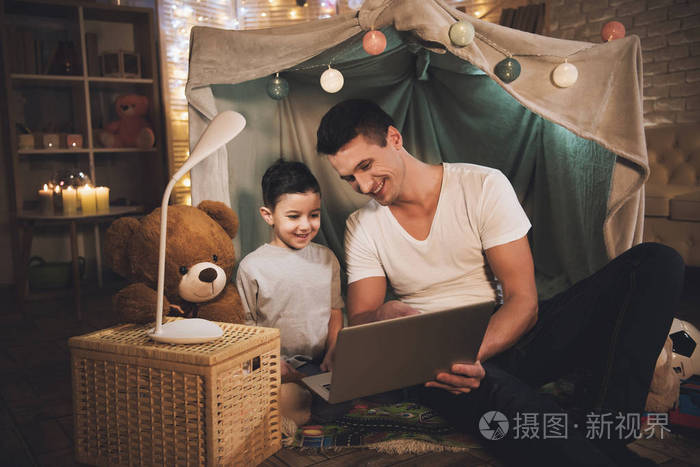 父亲和儿子在家里的沙发上看电影的笔记本电脑