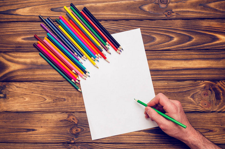 在一张木桌上, 手拿着彩色铅笔和一张白纸