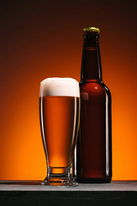 在橙色背景下关闭啤酒瓶和杯的视图